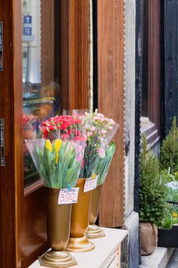 Avrupa 'da küçük bir çiçekçinin önünde sergilenen taze lale ve karanfillerden oluşan renkli buketler. Dekoratif vazolarda bahar çiçekleri sıcak ve davetkar bir sokak manzarası yaratır..