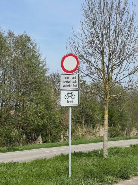 Alman yol tabelası, tarım / ormancılık trafiği ve bisikletler dışında, baharda bulutlu gökyüzü altında ağaçlarla kaplı kırsal bir yol kenarında araçları yasaklıyor..