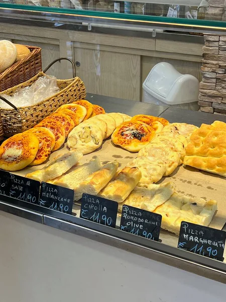 İtalyan pizza dilimleri ve Focaccia bir pastane tezgahında sergileniyor. Fiyat etiketleri, taze pişmiş sokak yemekleri ve bir şarküteri vitrininde atıştırmalıklar..