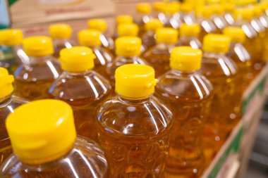 Süpermarkette raflarda sıralanmış parlak sarı kapaklı altın ayçiçeği yağı şişeleri. Alışveriş konsepti.