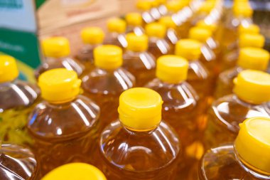 Süpermarkette raflarda sıralanmış parlak sarı kapaklı altın ayçiçeği yağı şişeleri. Alışveriş konsepti.