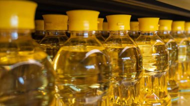 Süpermarkette raflarda sıralanmış parlak sarı kapaklı altın ayçiçeği yağı şişeleri. Alışveriş konsepti.