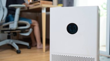 Beyaz hava temizleyicisi arka planda çalışan bir kadının hava kalitesi indeksini gösteriyor. Temiz hava ve sağlıklı ofis ortamı kavramı.