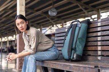 Güzel Asyalı sırt çantalı kadın trende bekleyen ceketli mavi sırt çantalı tren istasyonundan gelen treni seyrediyor..