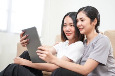 Sevgi LGBT konsepti. Mutlu Asyalı güzel lezbiyen çift yavaş çekimde oturma odasında konuşuyor ve tablet kullanıyor. Kaliteli zaman, eğlence, teknoloji ve aşk harcamak.