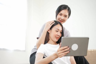 Sevgi LGBT konsepti. Mutlu Asyalı güzel lezbiyen çift yavaş çekimde oturma odasında konuşuyor ve tablet kullanıyor. Kaliteli zaman, eğlence, teknoloji ve aşk harcamak.