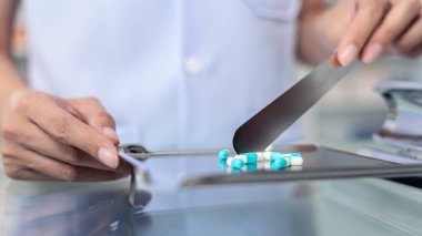 Kadın eczacıların sayımını kapat ve eczanedeki spatulayla birlikte kaliteli paslanmaz sayım tepsisine haplar yerleştir. Eczacı eczanede reçeteyle paslanmaz tepside ilaç hazırlıyor..