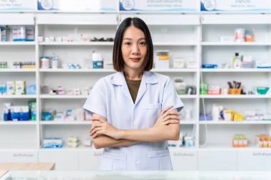 Kolları çapraz duran ve kameraya bakan mutlu Asyalı kadın eczacı eczanedeki işinden gurur duyuyor ve kendini iyi hissediyor..
