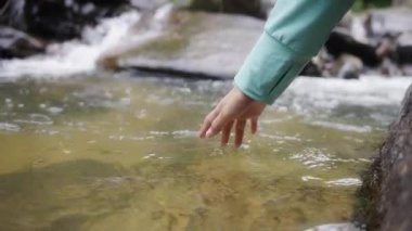 Bir kadının eli derelerin, nehirlerin ve şelalelerin yüzeyine değiyor. Rahatlamış ve dinlenmek için iyi hissediyor. İnsanlar doğanın ve hayatın tadını çıkararak seyahat ederler. Çözünürlük ve yavaş çekim..