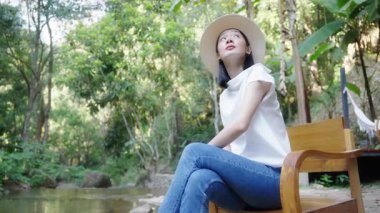 Şelalenin önündeki tahta koltukta oturan güzel Asyalı genç kadın tatilde temiz hava aldığı için kendini rahat ve mutlu hissediyordu..