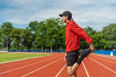 Genç Asyalı adam dışarıda koşuya çıkmadan önce bacağını ısıtıyor. Spor giyimli adam sabah sağlık ve refah için dışarıda egzersiz yapıyor..