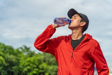 Koşu pistinde koştuktan sonra şişeden su içen yakışıklı Asyalı adam, dışarıda çalışma konsepti, koşudan sonra temiz maden suyu içmek. Z jenerasyonu yaşam biçimi.