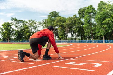 Genç Asyalı koşucu koşu parkurunda koşuya başlamak için başlangıç bloğunu kullanıyor, dışarıda egzersiz konseptini kullanıyor, koşudan sonra temiz maden suyu içiyor. Z jenerasyonu yaşam biçimi.