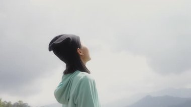 Yeşil ceketli Asyalı genç yürüyüşçü kadın gün batımında dağın zirvesine doğru koşuyor temiz hava soluyor, saçlar rüzgarda uçuşuyor, İnsan Dağları Özgürlük Kavramı, Mutluluk.