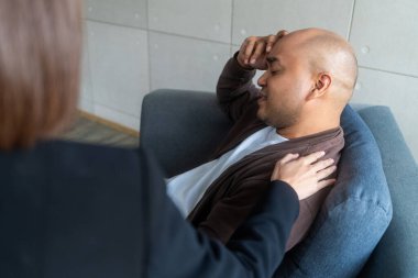 Asyalı adam, akıl sağlığı kliniğinde Asyalı kadın psikologla danışmanlık yapıyor. Psikolog konuşuyor ve depresyondaki erkek hastaya destek olmak için el ele tutuşuyor..