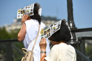 Paris, Fransa-25 Haziran 2025: İki Asyalı turist kafalarını Paris, Fransa 'daki bir müzeden gelen broşürlerle güneşten koruyor.