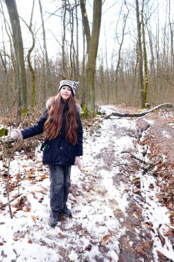 Uzun saçlı bir kız ormanda karlı bir yolda duruyor. O, kalın giysiler giydi. Etrafını saran ağaçlar ve her yer karla kaplı..