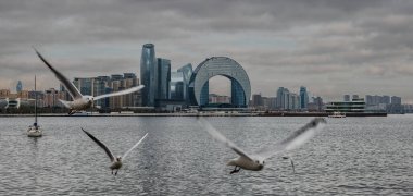 İkonik dairesel gökdelenli fütüristik kıyı şeridi. Crescent Körfezi, yelkenliler ve bulutlu gökyüzünün altında uçan kuşlar. Bakü, Azerbaycan.