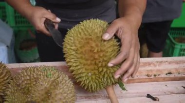 Meyve satıcısı markette bıçakla taze Durian kesiyor, geleneksel meyve sapı ve tropikal ürün sergiliyor.