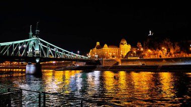Budapeşte, Macaristan - 12 Ekim 2025: Özgürlük Köprüsü ile Budapeşte 'nin manzaralı gece manzarası, tarihi nehir kenarı binaları ve Tuna Nehri üzerinde parıldayan yansımalar.