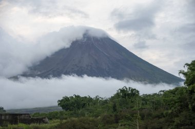 Merapi Dağı 'nın zirvesi kısmen sis ve bulutlarla örtülüdür. Aktif bir yanardağ kraterinden sık sık akkor lav yayar..