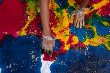 Plastik eldiven giyen biri bir parça beyaz bezi tekstil boyasıyla boyuyor. Kumaşı ortam olarak kullanarak el sanatlarında yaratıcılık.