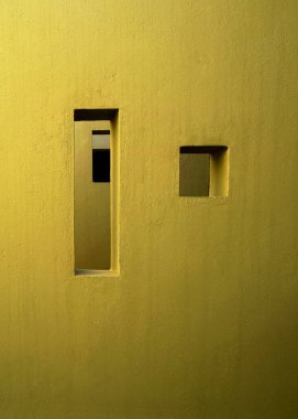 Dar bir dikey açıklık ve dokulu sarı bir duvar üzerinde kare bir oyuk içeren minimalist kentsel mimari detay