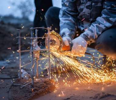 Bir insan gelecekteki beton bir yapı için destek kafesi kesiyor. Akşamları inşaat alanında. Yüksek kalite fotoğraf