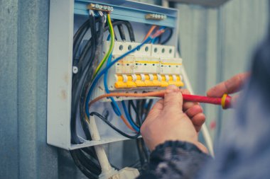 Elektrikçi elektrik panelindeki kabloları vidalıyor. Arka arkaya birkaç otomatik makine elektriği ve elektrikçinin ellerini kapattı. Yüksek kalite fotoğraf