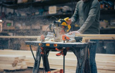 Profesyonel bir marangoz tahtayı dairesel testereyle keser. Dairesel testere, talaş, talaş ve sinek tozunun altından. Mobilya fabrikasında çalışıyorum. Yüksek kalite fotoğraf