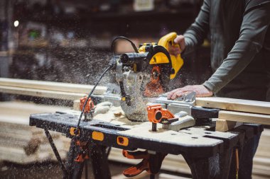 Profesyonel bir marangoz tahtayı dairesel testereyle keser. Dairesel testere, talaş, talaş ve sinek tozunun altından. Mobilya fabrikasında çalışıyorum. Yüksek kalite fotoğraf