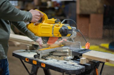 Profesyonel bir marangoz tahtayı dairesel testereyle keser. Dairesel testere, talaş, talaş ve sinek tozunun altından. Mobilya fabrikasında çalışıyorum. Yüksek kalite fotoğraf