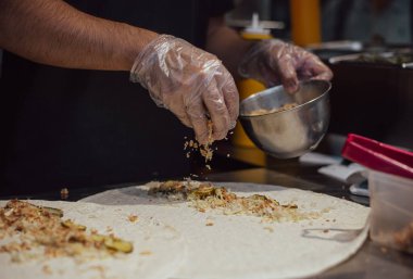 Fast food dükkanında yemek yaparken çekilmiş karanlık atmosferik bir fotoğraf. Tavuk eti pide ekmeğinde kaynatılır. Aşçının eldivenli elleri lezzetli sokak yemekleri yaratıyor. Yüzü yok. Masa ürünleri ve şef.
