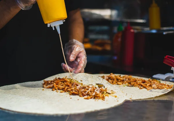 Sokak yemekleri pişirirken yemeğin üzerine ketçap dökülüyor. Şef tavuk etinin üzerine baharat döker. Akşam Eldivenli Eller Mutfakta Karanlık Arka plan Sokak Yemeği.