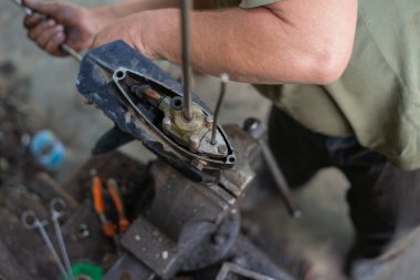 Uzman bir otomobil tamircisinin elleri. Dış motorda benzini tamir ediyor. Tamircinin elleri yağ ve tükürükle lekelenmiş. Çerçevede tekne ünitesinin pervanesi ve pompası var. Yüksek kalite fotoğraf