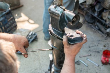 Uzman bir otomobil tamircisinin elleri. Dış motorda benzini tamir ediyor. Tamircinin elleri yağ ve tükürükle lekelenmiş. Çerçevede tekne ünitesinin pervanesi ve pompası var. Yüksek kalite fotoğraf