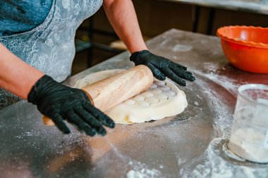Şirketin mutfağında gerçek bir çalışma ortamı. Yakın planda, siyah eldivenli eller hamuru merdaneyle çeviriyor, altıgen desenler oluşturuyor, bu da hamur köftesi üretme sürecini gösteriyor. Yüksek kalite fotoğraf