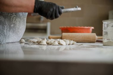 Yakın plan, metal bir yüzeyde hamur köftesi yapma sürecini gösteriyor, yanında hamurlu bir kalıp, merdane ve turuncu bir kase var. Pelmenias 'ın hızlı pişirilmesinin endüstriyel yöntemi