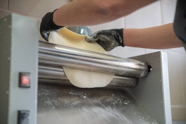 Yakın plan bir fotoğraf, profesyonel bir makinenin yardımıyla hamuru yuvarlama sürecini yakalar. Şef hamuru çıkarmak için hamuru iki paslanmaz çelik rulonun arasına koyar. Yüksek kalite fotoğraf