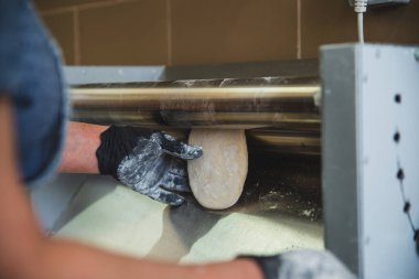 Yakın plan bir fotoğraf, profesyonel bir makinenin yardımıyla hamuru yuvarlama sürecini yakalar. Şef hamuru çıkarmak için hamuru iki paslanmaz çelik rulonun arasına koyar. Yüksek kalite fotoğraf