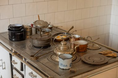 Bakır Mutfak Fırını ve Geleneksel Kızartma Tavası Sahnesi. Geleneksel yemek pişirme yüzeyinde bakır tencereli ve tavalı olan antika bir sobanın yakın görüntüsü. Tarihsel mutfak atmosferi işçiliğin altını çiziyor ve