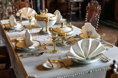 Porselen tabaklar, keten peçeteler ve tarihi bir iç mekânda klasik çatal bıçaklarla hazırlanmış lüks bir yemek masası. Rafine edilmiş atmosfer geleneği, görgü kurallarını ve zarif ev yemeklerini temsil ediyor. Yaşam tarzı, konukseverlik ve miras kavramları için mükemmel.