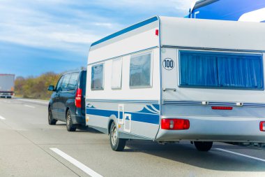 Seyahat sırasında bir karavanı çekerken otoyolda araba kullanmak. Görüntü yol gezisi yaşam tarzını, turizm hareketliliğini ve eğlence amaçlı seyahatleri temsil ediyor. Tatil gezisi, kamp kültürü ve aile tatili kavramları için uygundur..