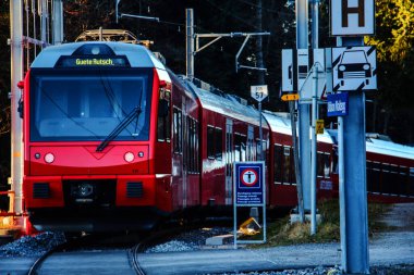 Kızıl İsviçreli yolcu treni kırsal demiryolu geçidine yanaşıyor.