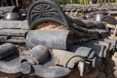Geleneksel Kore çatı kiremitleri ve dekoratif tepe detaylarını kırsal bir ortamda yakından görmek, eskimiş dokuyu, işçiliği ve Kore mimari mirasını vurgulamak..