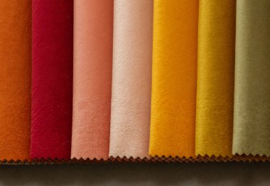 Döşeme kumaşı örnekleri turuncu, pembe, kırmızı, sarı ve zeytin yeşili tonlarını içeren sıcak renk paletinde sergilenmektedir. Kumaşlar dikey olarak dizilmiş, yumuşak parıltılı yumuşak, kadife bir doku sergiliyorlar..