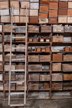 Ahşap raflar eski karton ve ahşap kutularla dolu. Kutular bej ve kahverenginin tonlarında değişir ve tekrarlanan geometrik desenler yaratır..