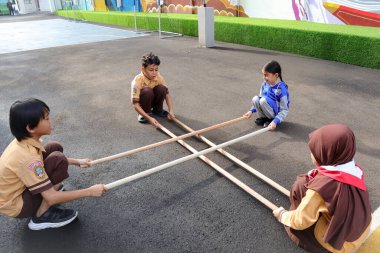 İlkokul çocukları dışarıda geleneksel bambu oyunu oynuyorlar..