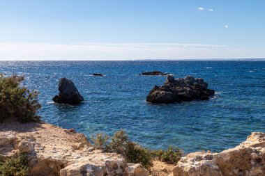 Alicante yakınlarındaki Tabarca Adası 'nda berrak mavi suyu olan kayalık bir kıyı şeridi. Parlak bir gökyüzü altında denizden yükselen birkaç kaya oluşumu, sakin bir Akdeniz kıyı manzarası yaratıyor..