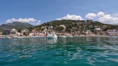 Mallorca Adası 'ndaki Port de Soller manzaralı sakin mavi suları, demirlemiş tekneleri ve yeşil tepeler ve dağlarla çevrili bir sahil kasabasını gösteriyor..